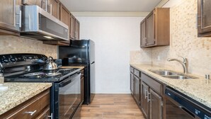 A kitchen with wooden cabinets, a stainless steel refrigerator, a black stove, granite countertops, and a granite backsplash. - Mountainside Inn 122 1 Bedroom Condo by Alpine Lodging Telluride (Telluride)