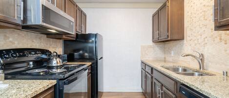 Eine Küche mit Holzschränken, einem Edelstahl-Kühlschrank, einem schwarzen Herd, Granit-Arbeitsplatten und einer Granit-Spritzschutzwand.