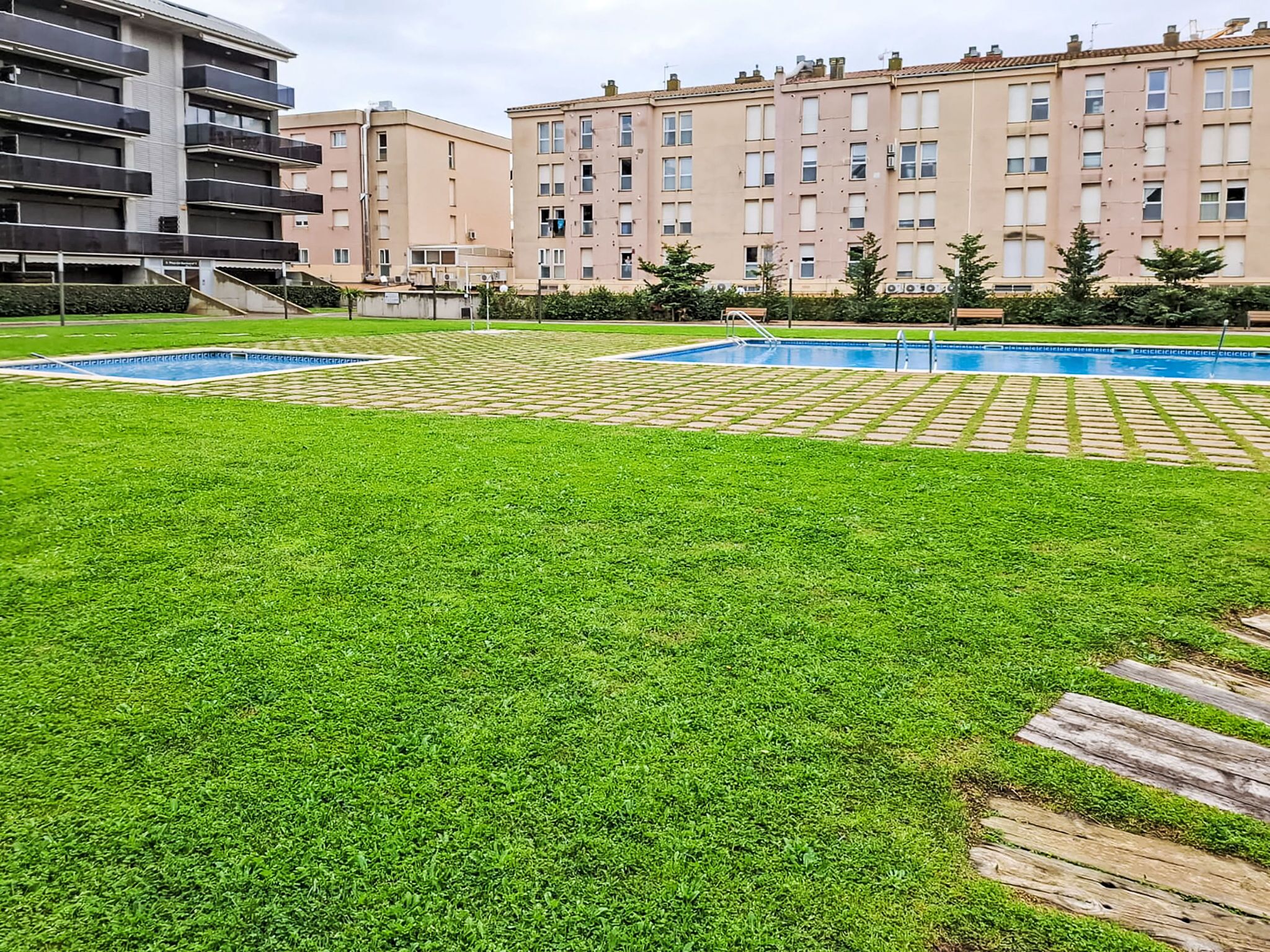 A residential area with a swimming pool, green lawn, and apartment buildings in the background.