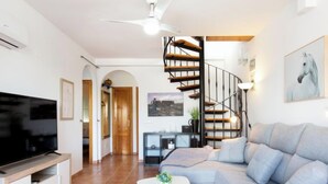 A modern living room with a large flat-screen TV, a grey sofa, a white coffee table, and a spiral staircase. - Apartment Velez by Interhome (Nerja)