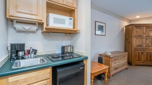 A compact kitchen with wooden cabinets, a microwave, a coffee maker, a sink, and a small refrigerator.