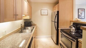 A compact kitchen with wooden cabinets, a stainless steel refrigerator, a stove, and a microwave. - Mountainside Inn 106 1 Bedroom Condo by Alpine Lodging Telluride (Telluride)