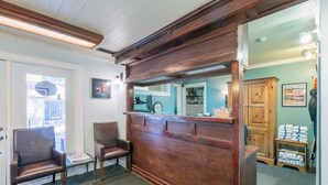 A reception area with a wooden reception desk, two leather chairs, a small table, and a view of the outside through a door. - Mountainside Inn 106 1 Bedroom Condo by Alpine Lodging Telluride (Telluride)