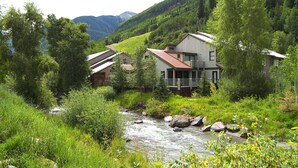 A house with a porch overlooking a river, surrounded by lush greenery and mountains in the background. - Mountainside Inn 106 1 Bedroom Condo by Alpine Lodging Telluride (Telluride)