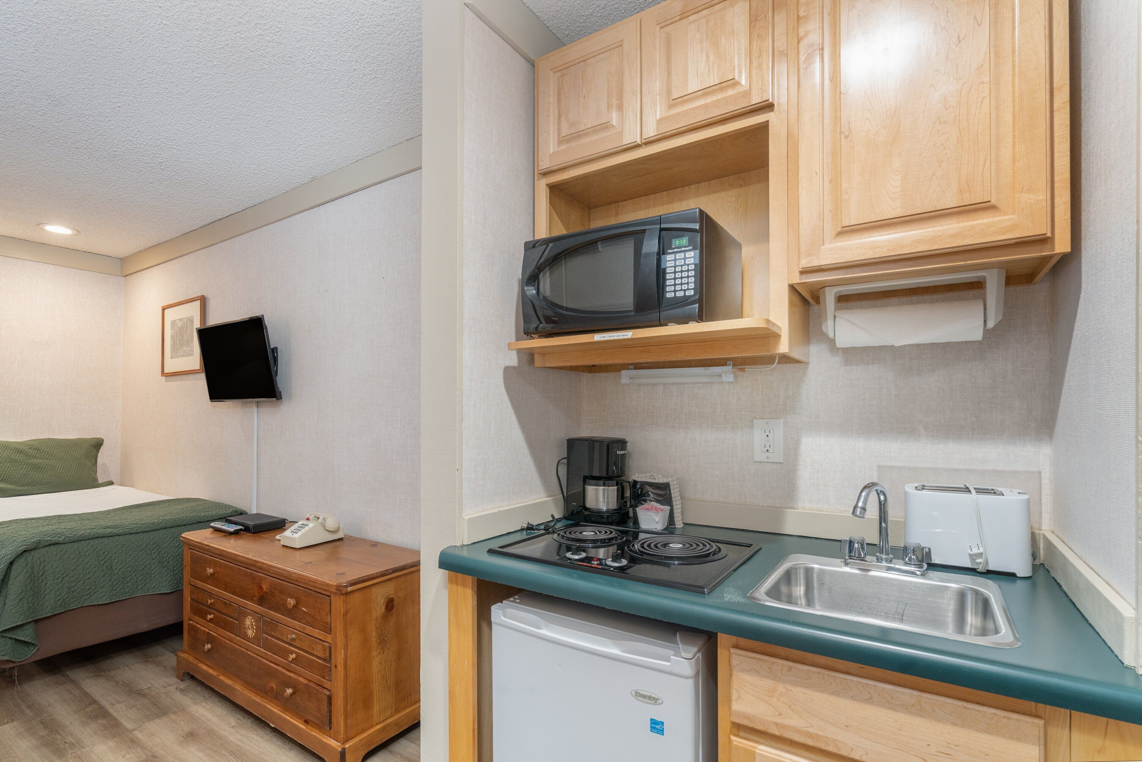 A compact kitchen with a microwave, stove, sink, and a small refrigerator.