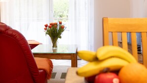A living room with a glass table, a vase of flowers, a red chair, and a bowl of fruit. - Sonnenküste by Interhome (Trassenheide)