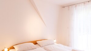A bedroom with a wooden headboard, two white beds, a bedside lamp, and a window with sheer curtains. - Sonnenküste by Interhome (Trassenheide)