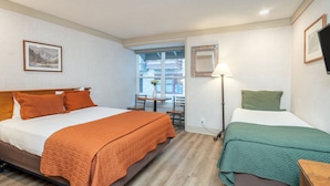 Quarto de hotel com uma cama grande, uma cama menor, uma escrivaninha e uma janela com vista para edifícios.