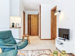 Un salon avec un fauteuil turquoise, une porte en bois, un téléviseur et une petite table sur laquelle se trouve une bouilloire.
