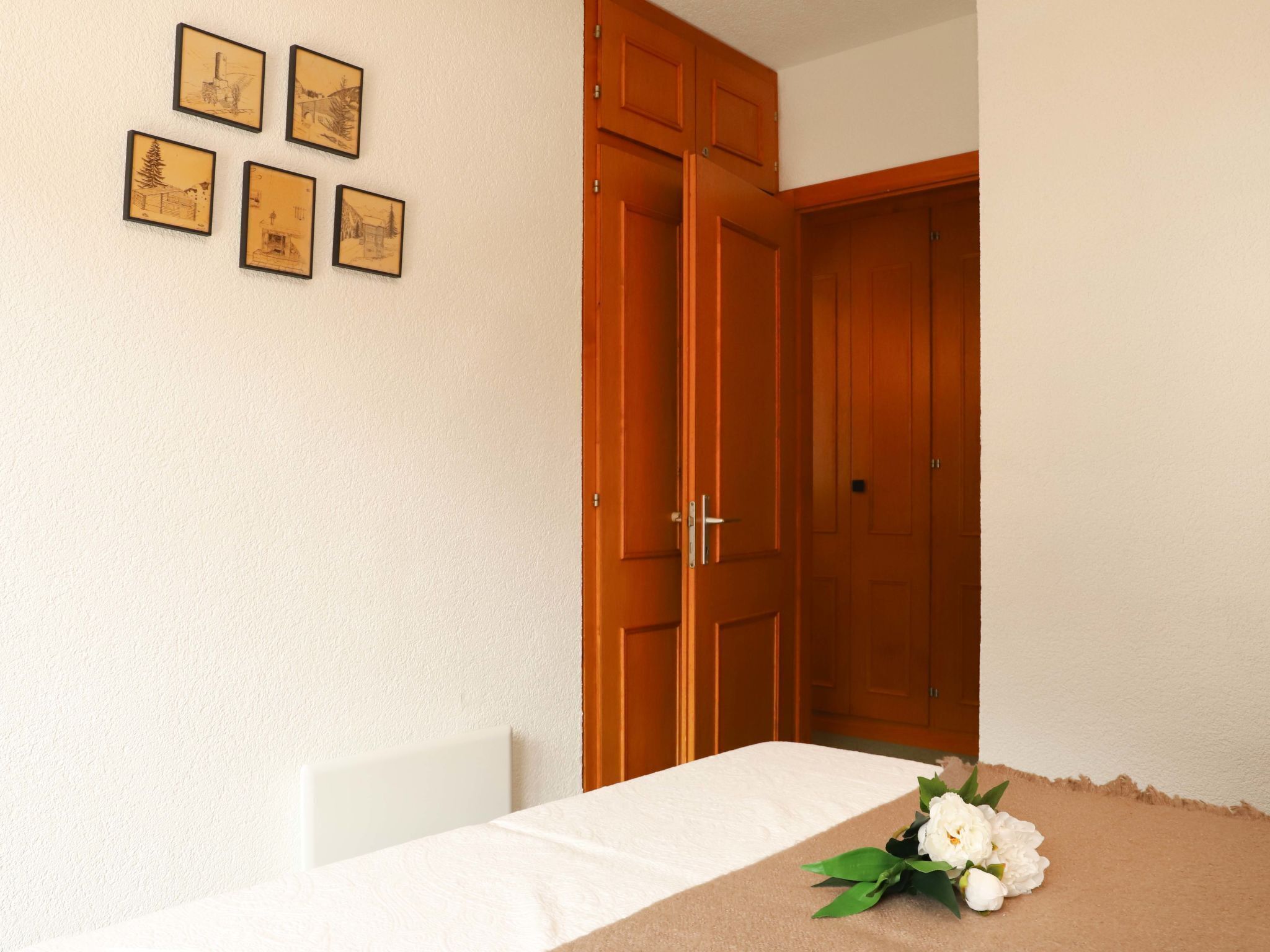 Ein Zimmer mit einem Holzschrank, einem weißen Tisch und vier gerahmten Bildern an der Wand.