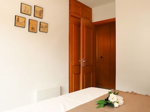A room with a wooden wardrobe, a white table, and four framed pictures on the wall.