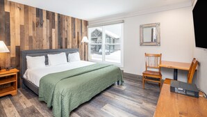 A bedroom with a bed, wooden floor, a window with a view, a desk, and a chair.