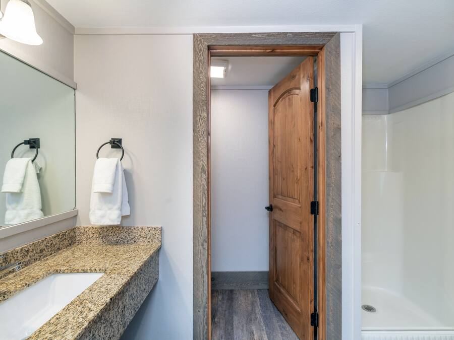 Un baño con lavamanos de encimera de granito, puerta de madera y cabina de ducha de vidrio.