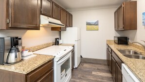 A compact kitchen with wooden cabinets, a built-in microwave, a coffee maker, a toaster, and a refrigerator. - Mountainside Inn 113 1 Bedroom Condo by Alpine Lodging Telluride (Telluride)