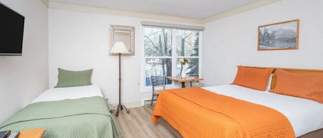 Une chambre avec deux lits, un bureau, une chaise, une lampe et une fenêtre donnant sur des arbres.