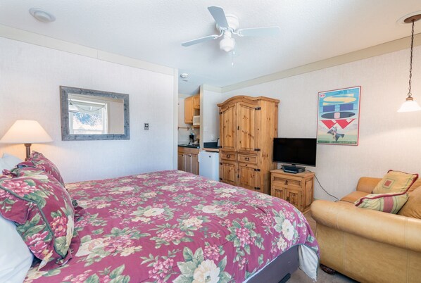Quarto com cama, televisão, aparador de madeira e ventoinha no teto.