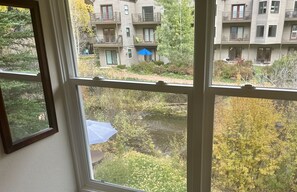A view through a window of a residential area with multiple balconies, a small body of water, and a garden with yellow foliage. - Mountainside Inn 221 1 Bedroom Hotel Room by Alpine Lodging Telluride (Telluride)