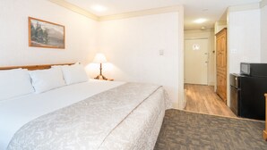 A hotel room with a bed, a lamp, a painting on the wall, a television, and a refrigerator. - Mountainside Inn 309 1 Bedroom Hotel Room by Alpine Lodging Telluride (Telluride)