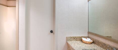 Ein Badezimmer mit einer weißen Tür, einer Arbeitsplatte aus Granit, einem Waschbecken und einem Spiegel.