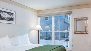 A hotel room with a bed, a window with a view of the outside, a framed picture on the wall, and a decorative mirror. - Mountainside Inn 210 1 Bedroom Hotel Room by Alpine Lodging Telluride (Telluride)