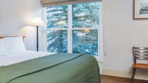 A hotel room with a bed, a chair, a window with a view of snow-covered trees, and a framed picture on the wall. - Mountainside Inn 211 1 Bedroom Hotel Room by Alpine Lodging Telluride (Telluride)