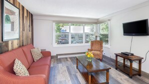 A living room with a red sofa, a patterned armchair, a wooden coffee table, and a television on a stand. - Mountainside Inn 222 1 Bedroom Condo by Alpine Lodging Telluride (Telluride)