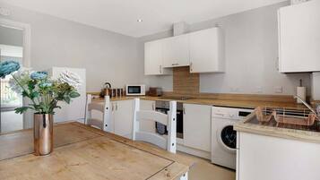 Een moderne keuken met witte kastjes, een houten aanrecht, een spoelbak, een magnetron en een wasmachine.