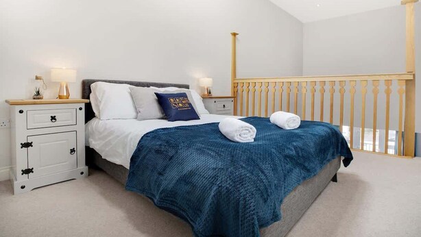 A bedroom with a bed, nightstands, a blue blanket, and a wooden railing. - Duplex apartment, close to A1, private car park (Darlington)
