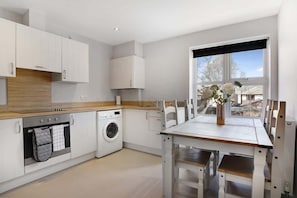 Una cocina moderna con armarios blancos, horno empotrado, lavadora y una mesa de comedor con sillas.