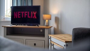 A television on a wooden stand with the word 'NETFLIX' on the screen, a lamp, and a chair. - Duplex apartment, close to A1, private car park (Darlington)