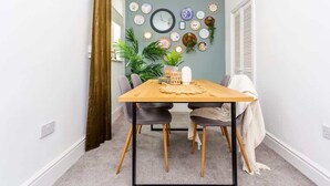 A dining area with a wooden table, two chairs, a wall clock, and various decorative plates.