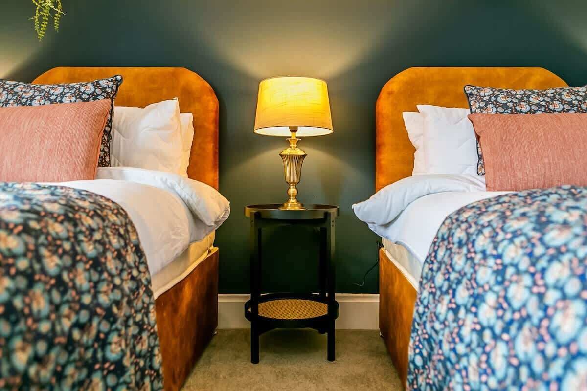 Een kamer met twee bedden, een tafeltje met een lamp en een donkergroene wand.