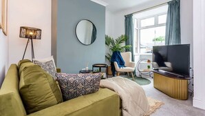 A living room with a sofa, a television, a round mirror, and a lamp.