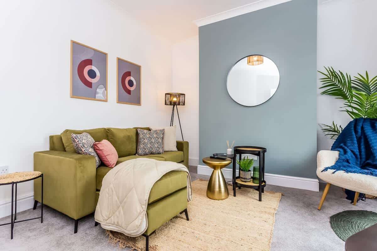 Ein modernes Wohnzimmer mit einem grünen Sofa, einem runden Spiegel und abstrakter Kunst an der Wand.