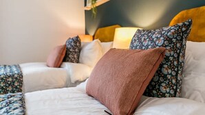 A bed with white bedding, a brown throw pillow, and a floral-patterned pillow.