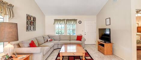 A living room with a sectional sofa, a wooden coffee table, a TV stand, and a patterned rug.