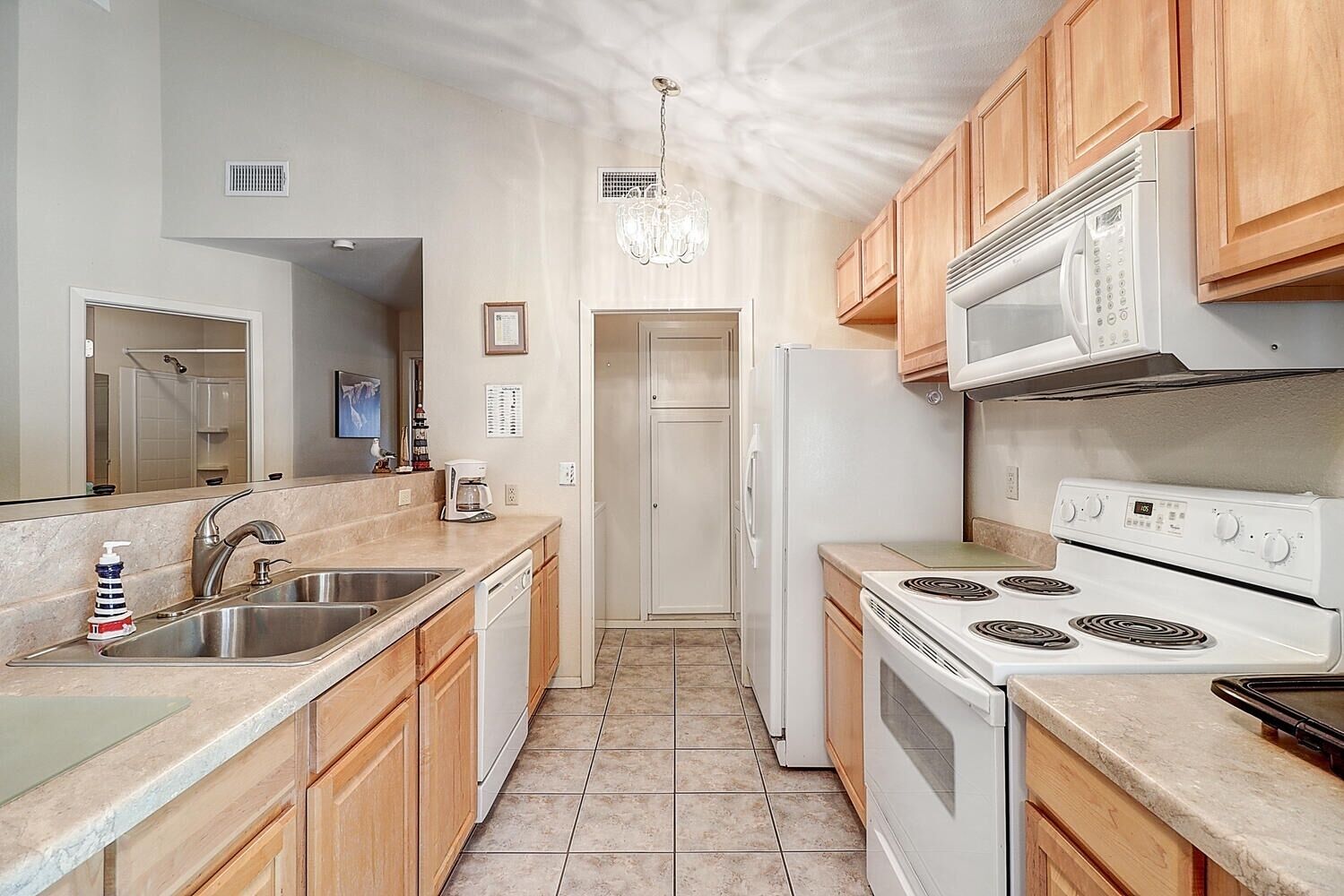 Una cocina con gabinetes de madera, un lavamanos de acero inoxidable, un refrigerador blanco, una estufa y un microondas.