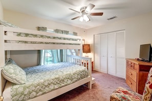A bunk bed room with a ceiling fan, a desk with a chair, a TV, and a wardrobe.