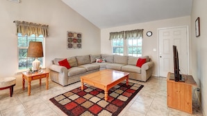 A living room with a sectional sofa, a wooden coffee table, a patterned rug, a lamp, a side table, and a television on a stand. - Seashell Memories 2 Bedroom Home by RedAwning (Rockport)