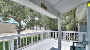 A covered porch with white railings, a green chair, and a view of a fenced yard with trees. - Seashell Memories 2 Bedroom Home by RedAwning (Rockport)