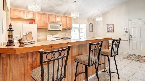 A kitchen with wooden cabinets, a microwave, a stove, and a bar area with two chairs. - Seashell Memories 2 Bedroom Home by RedAwning (Rockport)