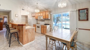 A kitchen with wooden cabinets, a central island with bar stools, a dining table, and a large window providing a view of the outdoors. - Seashell Memories 2 Bedroom Home by RedAwning (Rockport)