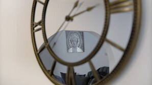 A wall clock with Roman numerals and a reflection of a room with a couch and pillows. - Family House near Durham & Newcastle (County Durham)