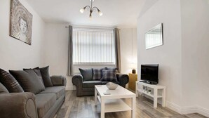 A living room with a sofa, a coffee table, a TV, and a window with blinds. - Family House near Durham & Newcastle (County Durham)