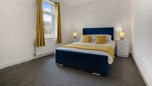 A bedroom with a bed, two bedside tables, a window with curtains, and a radiator. - Family House near Durham & Newcastle (County Durham)