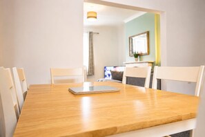 A dining table with chairs, a laptop, and a television in the background.