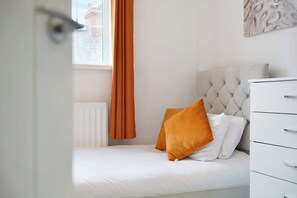 Een slaapkamer met een bed, een witte dressoir en een raam met gordijnen.