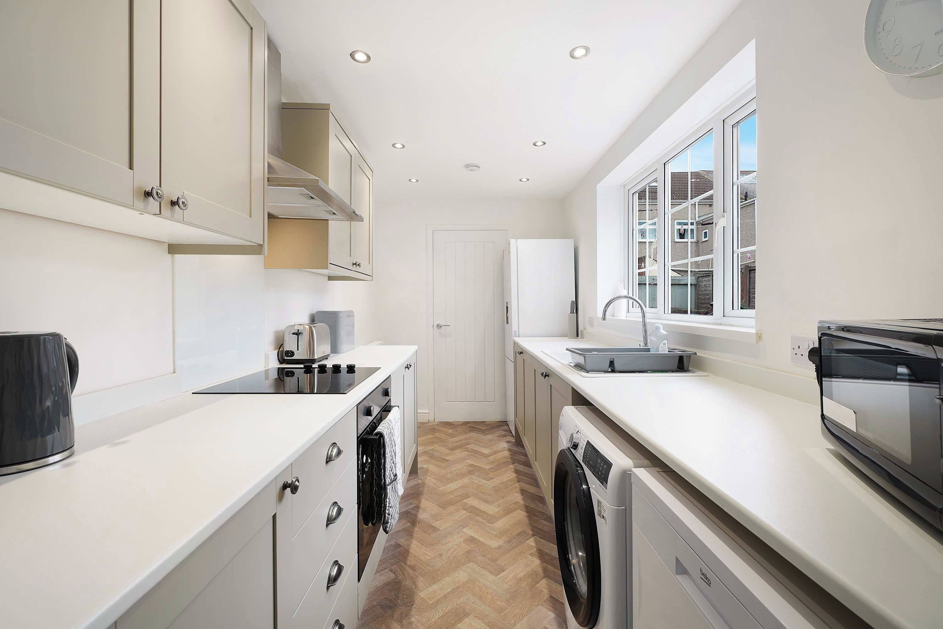 A modern kitchen with white cabinetry, a built-in oven, a dishwasher, and a window providing natural light.