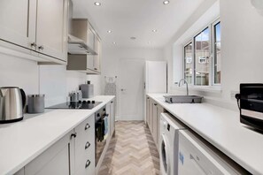 A modern kitchen with white cabinetry, a built-in oven, a washing machine, and a window with a view of the outside.