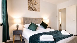 A hotel room with a large bed, two nightstands, a headboard, a painting, and a door.